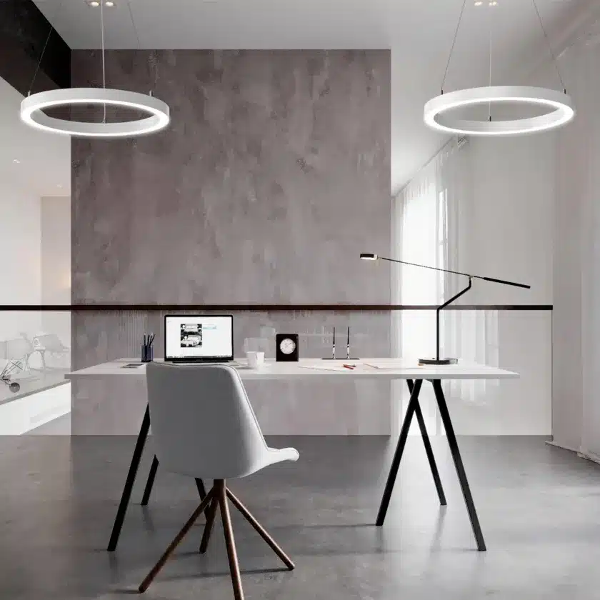 Contemporary office workspace featuring suspended circular LED pendant lights for modern architectural workplace lighting.